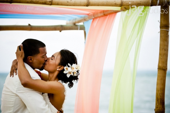 Newlyweds sharing a romantic kiss under a colorful wedding arch