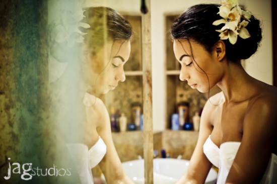A bride gazes at her reflection with flower hairpiece in bathroom