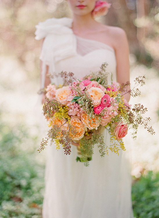 Bride in white gown holding peach and pink floral bouquet