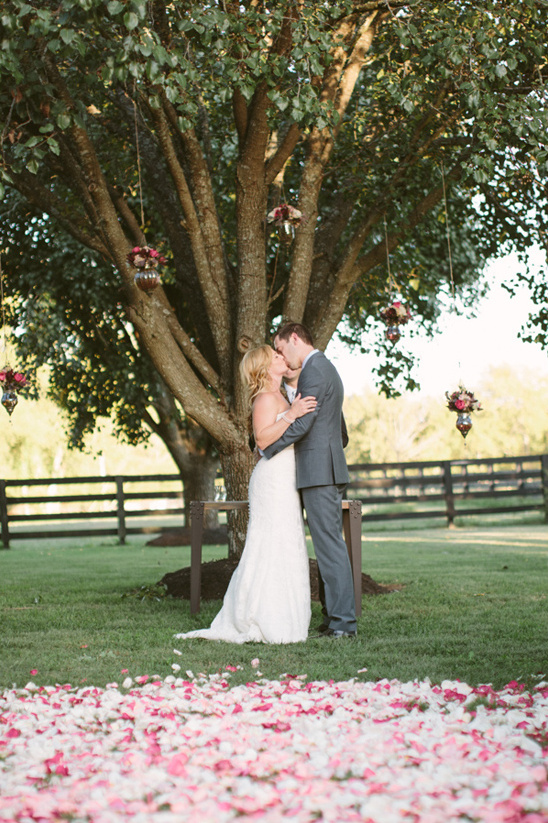 Bride and groom kissing under decorated tree at wedding