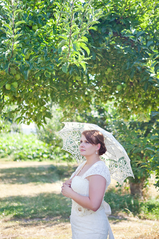 Bride holding parasol under apple tree gazing upward