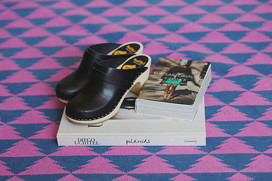 Black leather clogs with books on a patterned rug