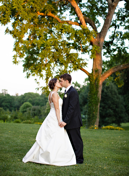 Bride and groom kiss under a tree on wedding day