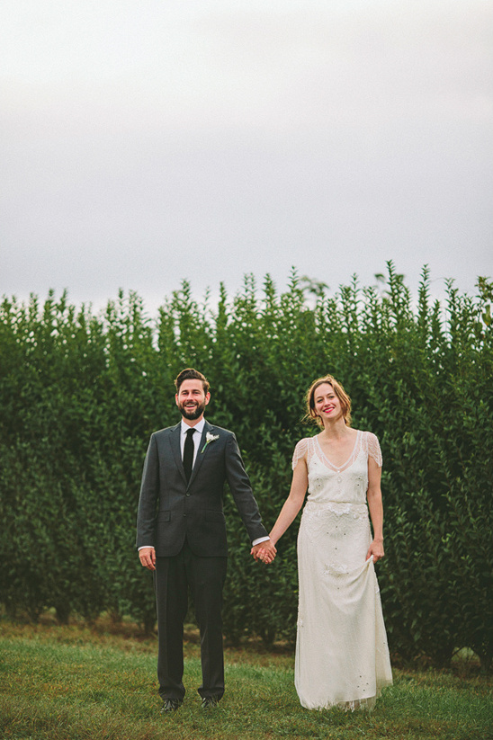 Newlyweds hold hands in front of greenery on their wedding day