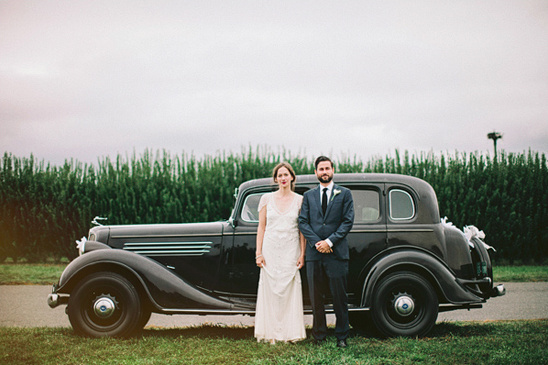 Happy couple posing by vintage car for wedding photo