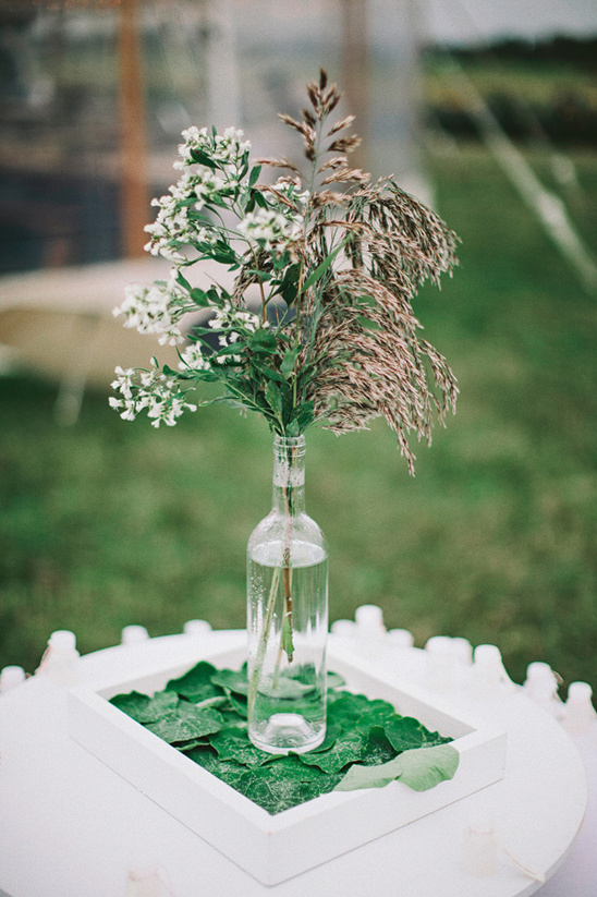 White flowers and grasses in glass bottle on tray