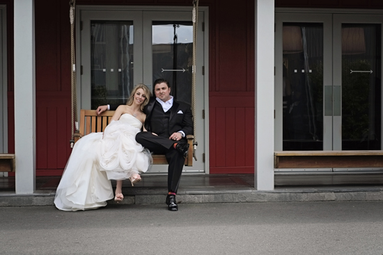 Newlyweds relax on a porch swing in wedding attire