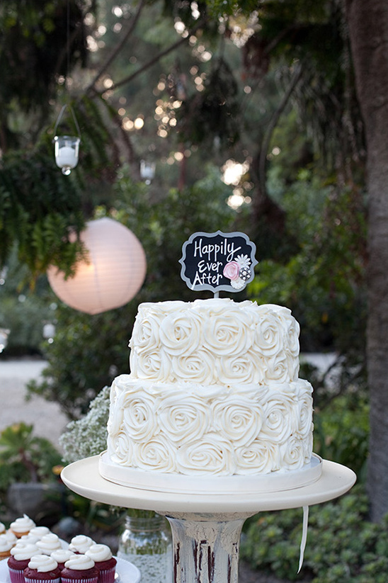 Two-tiered white wedding cake with a Happily Ever After sign
