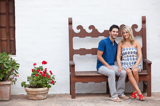 Couple sitting on a bench with red flowers in front of them