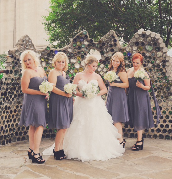 Bride and bridesmaids pose by bottle wall on wedding day