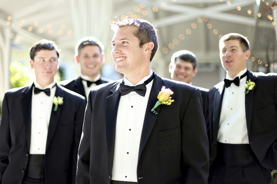 Groom and groomsmen in tuxedos smile at wedding