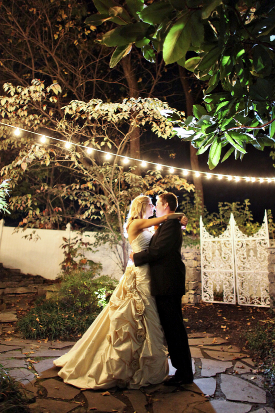 Bride and groom embracing under string lights at night