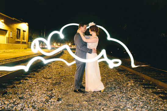 Romantic couple embraces amidst light-painted clouds on train tracks
