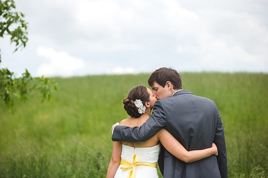 Bride and groom kiss in green field wedding photo