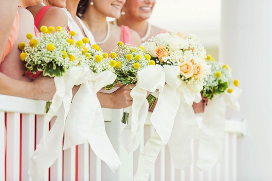 Bridesmaids holding colorful wedding bouquets with white ribbons