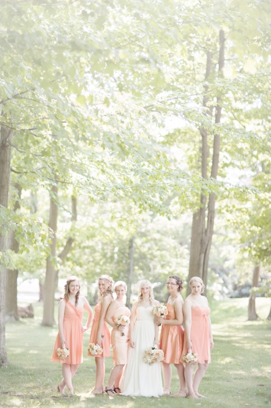 Bride and bridesmaids in peach dresses under leafy trees