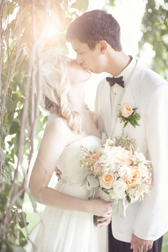 Romantic wedding kiss under sunlight with bouquet in hands