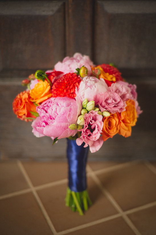Vibrant bridal bouquet with pink peonies and orange roses, tied with blue
