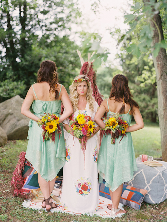 Boho bride with bridesmaids holding sunflower bouquets at an outdoor wedding