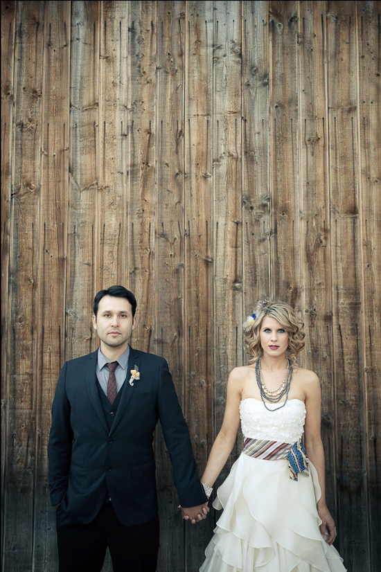 Newlyweds holding hands in front of a rustic wooden wall