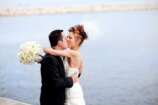 Bride and groom share a romantic kiss by the water on their wedding day