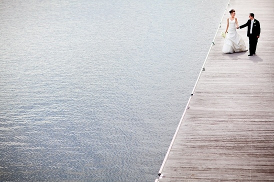 Bride and groom holding hands on a pier overlooking water