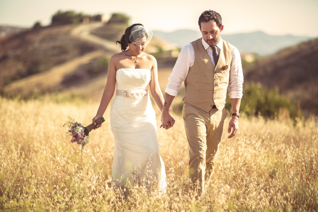 Newlyweds holding hands walking in a golden field on their wedding day