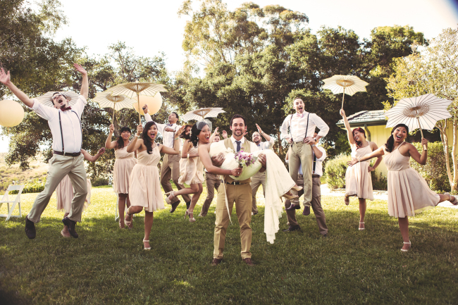 Joyful wedding group celebrates with dancing and parasols on a sunny day