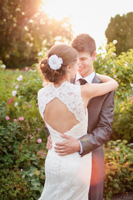 Bride and groom embrace in garden, sunset