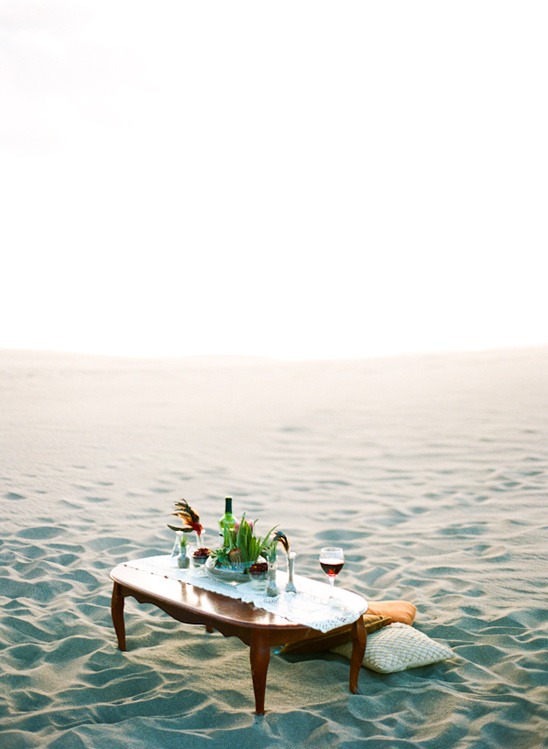 Romantic picnic setup with wine glasses on a sandy beach