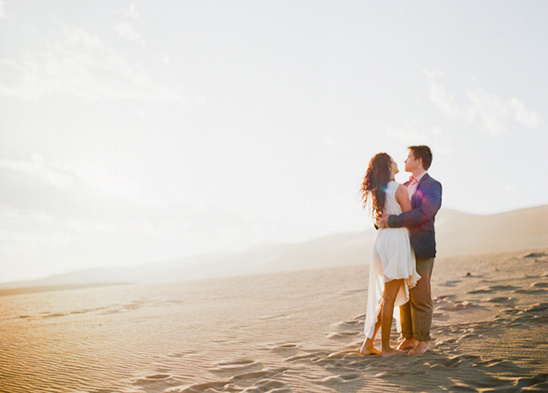 Couple embraces in the desert during golden hour with the sun behind them