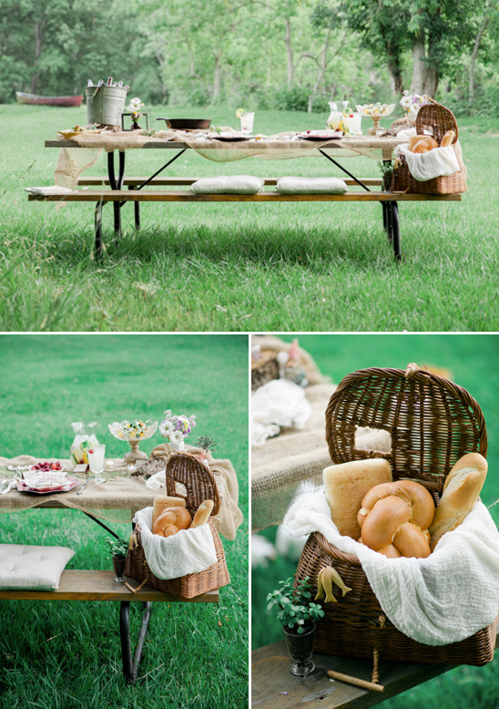 Picnic table set with food and bread baskets in a grassy field