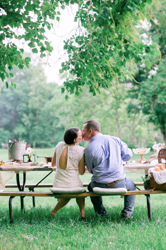 Couple kissing at picnic table in green grass during daytime