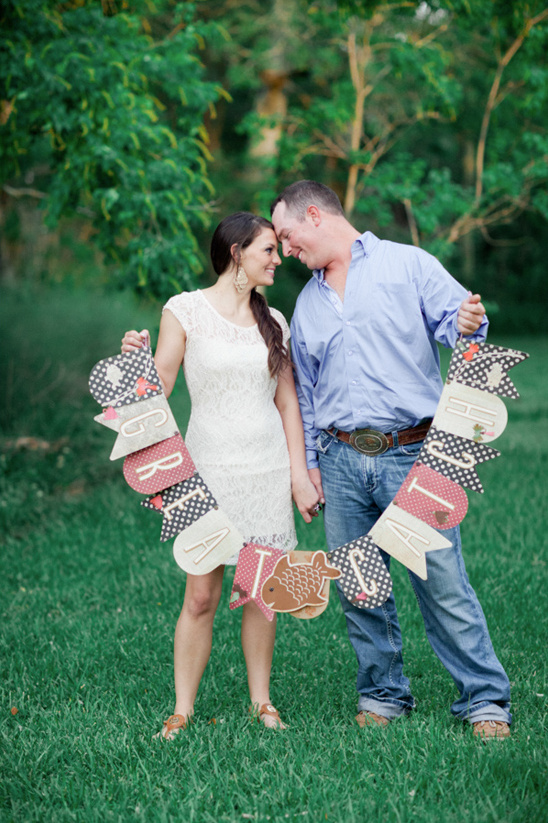 Couple celebrating engagement with a decorative frame outdoors in a park