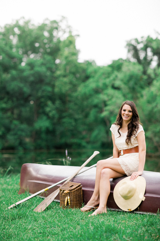 Young woman smiles near a canoe on a grassy lakeside
