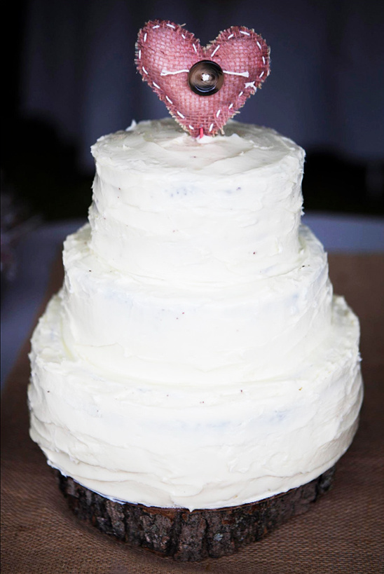 Rustic three-tiered wedding cake with heart topper on wooden base