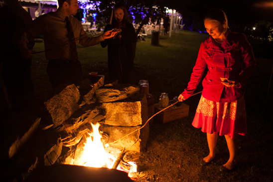 People gather around a bonfire, roasting marshmallows at night