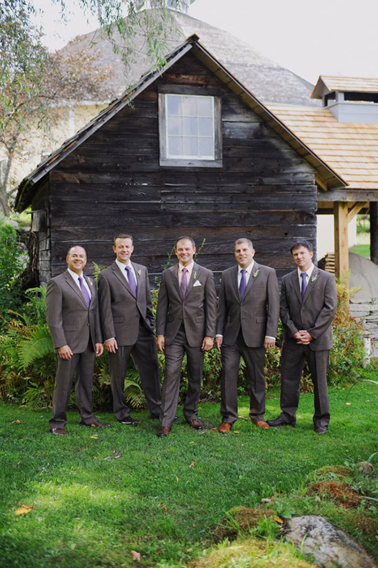 Groomsmen in suits posing for a photo in front of a barn