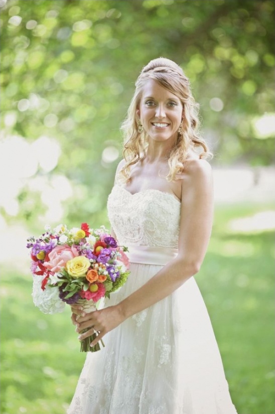 Smiling bride in white lace dress holding colorful bouquet