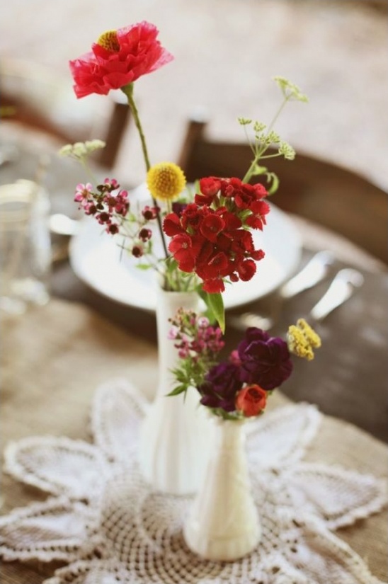 Small vases hold colorful flowers on a lace doily table