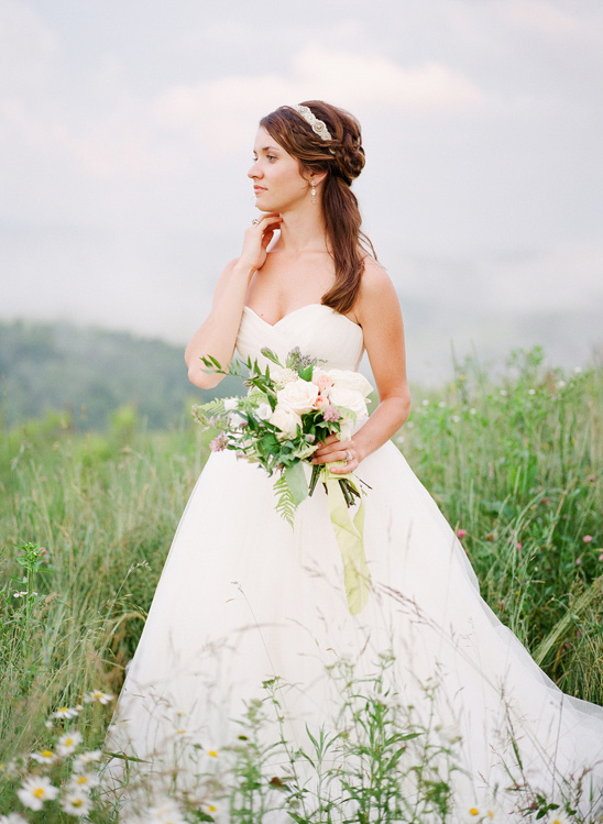 Bride in white dress holding bouquet in meadow