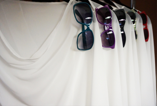 Colorful sunglasses hanging on white fabric display