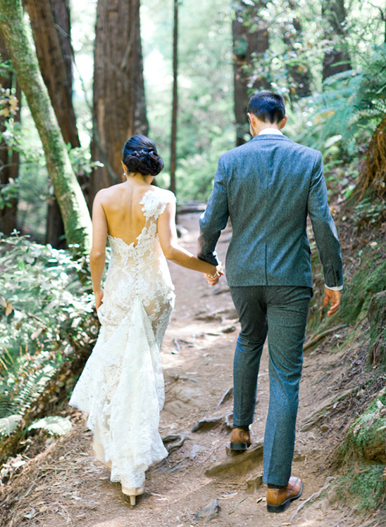 Newlyweds walk hand in hand through a forest trail