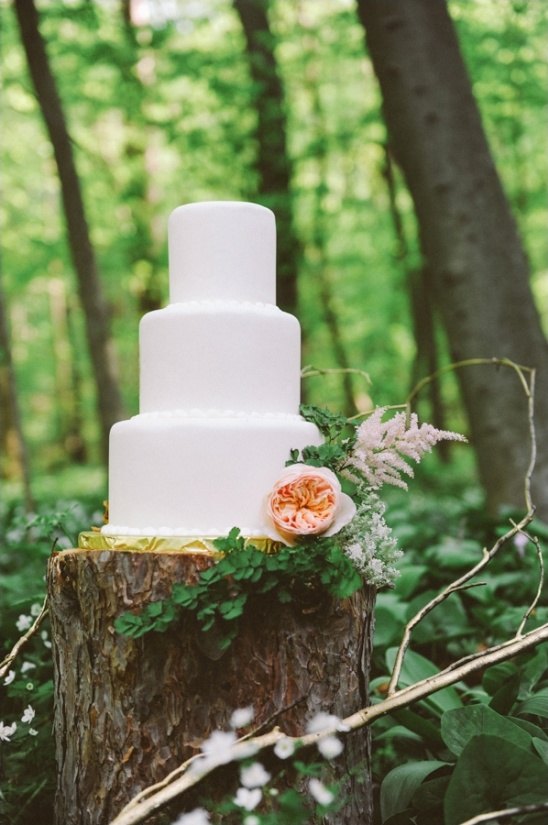 White wedding cake with flowers on a wood stump in forest