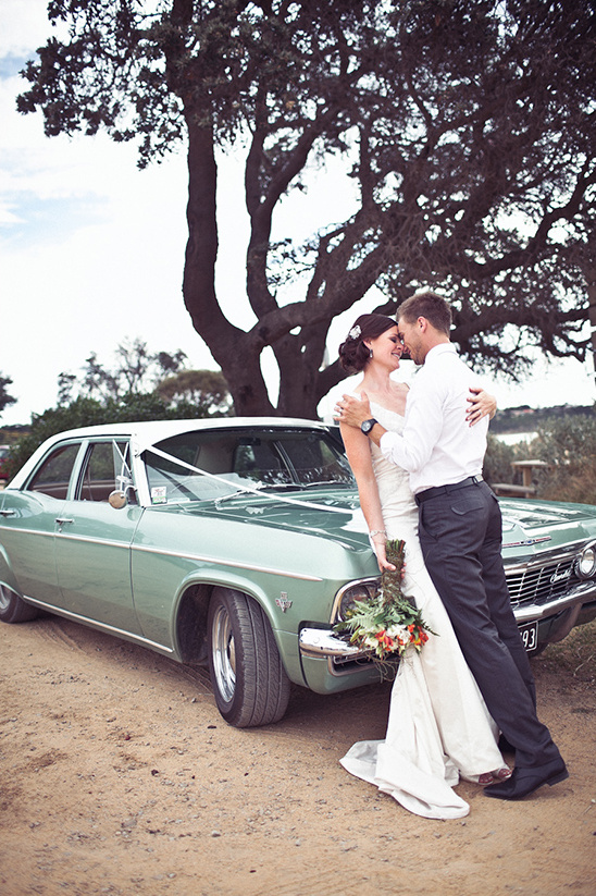 Bride and groom embrace by classic vintage car