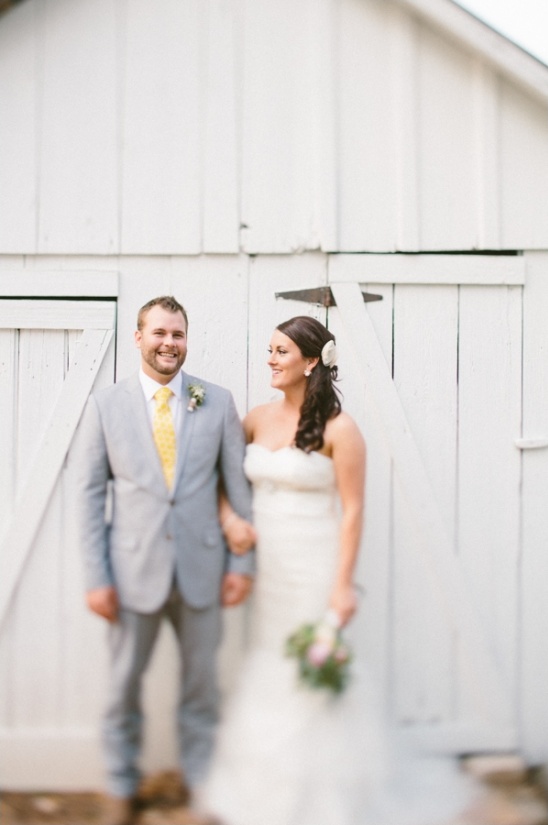 Happy bride and groom pose by white barn