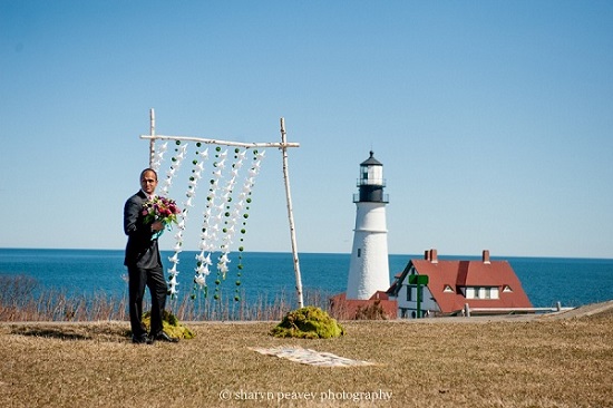 Groom standing by oceanside wedding arch near lighthouse