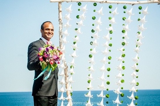 Groom holding bouquet by oceanside wedding backdrop