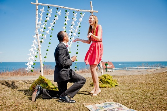 Man proposing to surprised woman by ocean