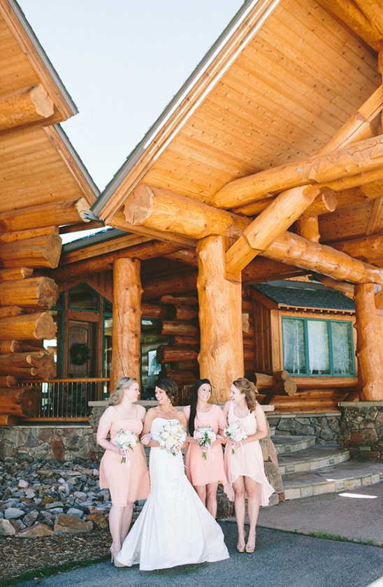 Bride and bridesmaids pose at rustic log cabin wedding